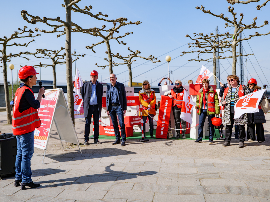 GEW NRW-Vorsitzende Ayla Çelik hält eine Rede vor der Baustelle Bildung. Viele Kolleg*innen und Politiker*innen hören zu.